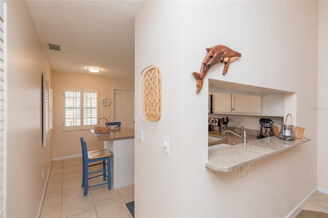 kitchen featuring a kitchen bar, light tile patterned floors, light stone counters, kitchen peninsula, and a textured ceiling