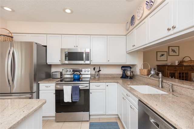 kitchen with sink, stainless steel appliances, light stone counters, a textured ceiling, and white cabinets