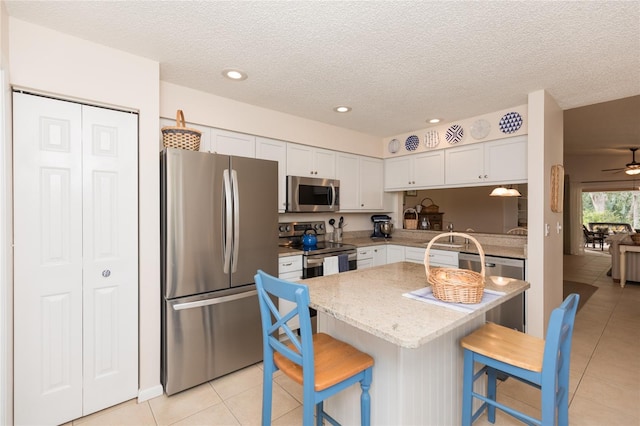 kitchen with white cabinets, a kitchen breakfast bar, a center island, stainless steel appliances, and light stone countertops