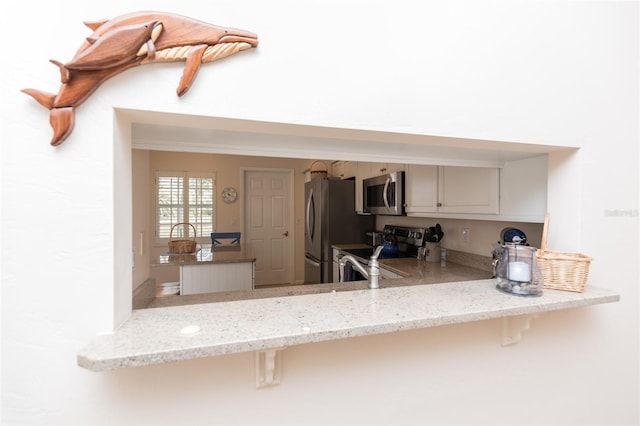 kitchen featuring stainless steel appliances, light stone countertops, and kitchen peninsula