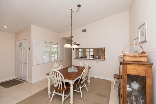 tiled dining space featuring vaulted ceiling and a textured ceiling