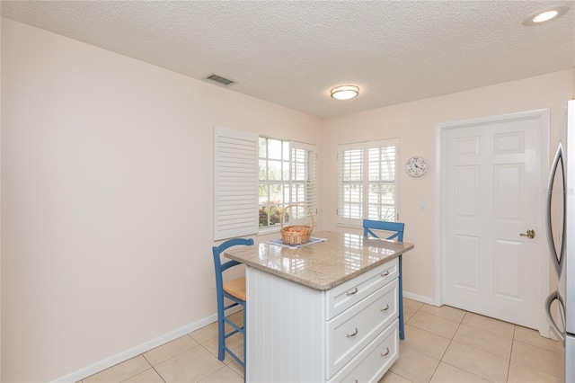 kitchen featuring light tile patterned flooring, white cabinetry, a breakfast bar area, a center island, and light stone countertops