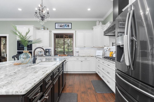 kitchen with sink, appliances with stainless steel finishes, white cabinetry, ornamental molding, and an island with sink