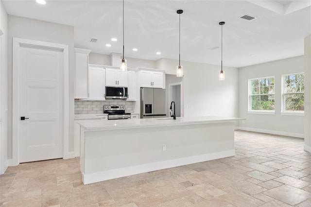 kitchen featuring pendant lighting, appliances with stainless steel finishes, white cabinetry, a center island with sink, and decorative backsplash