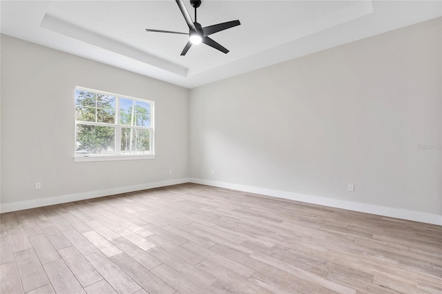 empty room with ceiling fan, light hardwood / wood-style floors, and a tray ceiling