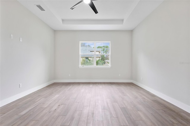 empty room featuring ceiling fan, a raised ceiling, and light wood-type flooring