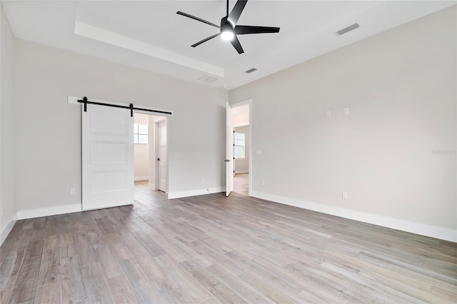 empty room with light hardwood / wood-style flooring, a barn door, and ceiling fan