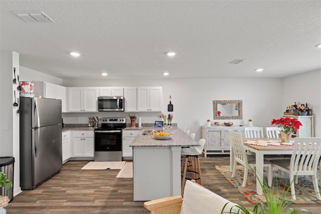 kitchen with a kitchen bar, white cabinetry, light stone counters, a kitchen island, and stainless steel appliances