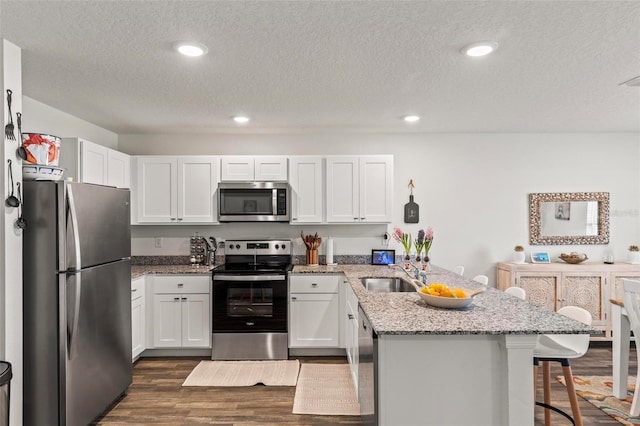 kitchen with sink, a breakfast bar, white cabinetry, stainless steel appliances, and light stone counters