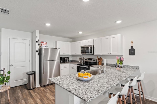 kitchen featuring white cabinetry, stainless steel appliances, kitchen peninsula, and a kitchen bar