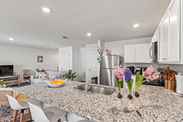 kitchen with a breakfast bar, white cabinetry, sink, light stone counters, and stainless steel appliances