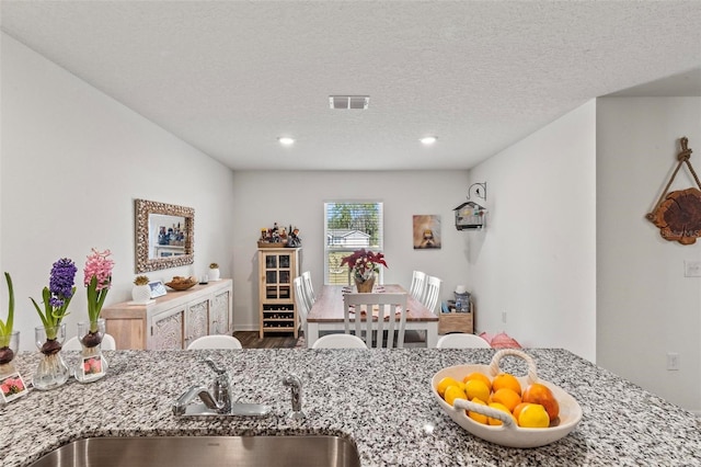 kitchen with sink, hardwood / wood-style floors, a textured ceiling, and light stone counters