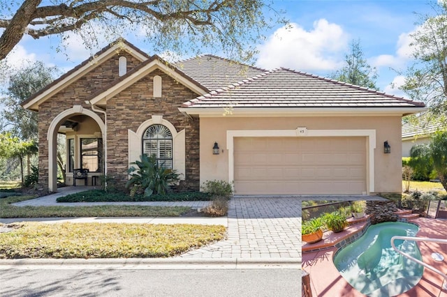 view of front of house featuring a garage, a tile roof, stone siding, decorative driveway, and stucco siding