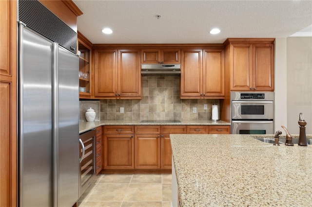 kitchen featuring sink, stainless steel appliances, light stone counters, tasteful backsplash, and a textured ceiling