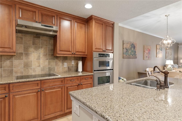 kitchen with light stone counters, black electric cooktop, sink, and hanging light fixtures