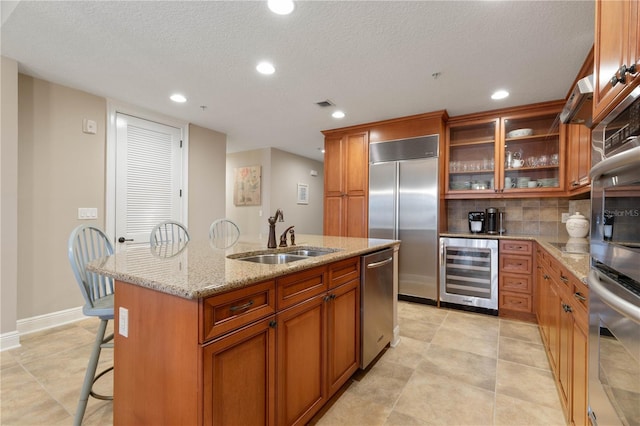 kitchen with sink, a breakfast bar area, wine cooler, stainless steel appliances, and a center island with sink