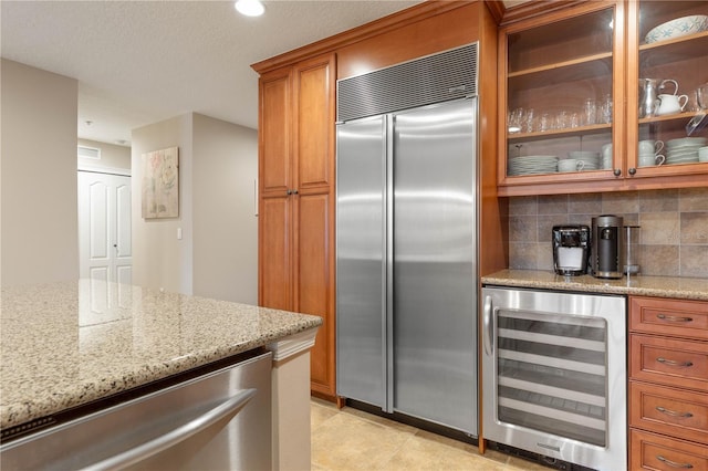 kitchen with stainless steel appliances, wine cooler, light stone countertops, a textured ceiling, and decorative backsplash