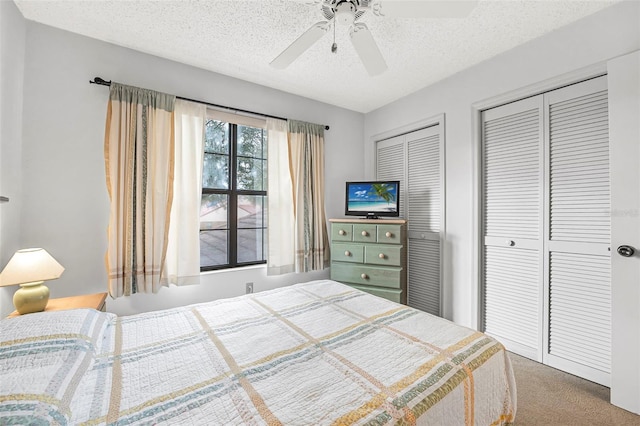 carpeted bedroom with ceiling fan, a textured ceiling, and two closets