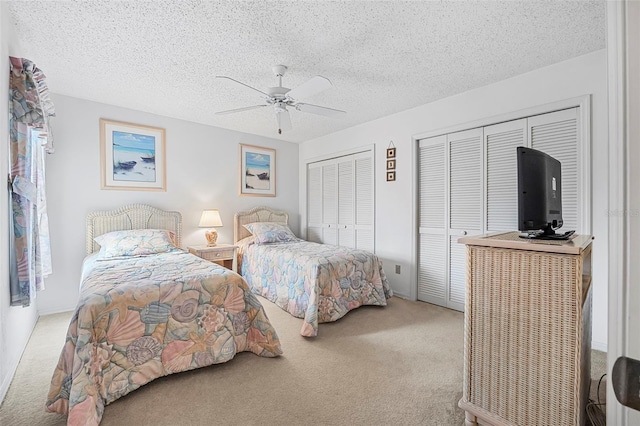 bedroom with multiple closets, light colored carpet, ceiling fan, and a textured ceiling