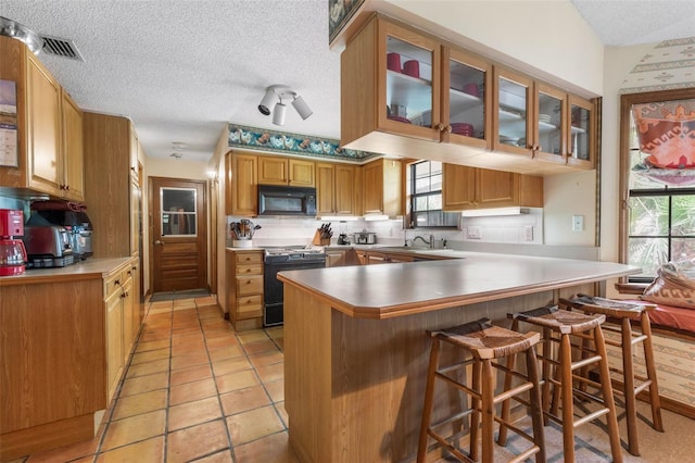 kitchen with sink, a breakfast bar area, stove, kitchen peninsula, and a textured ceiling