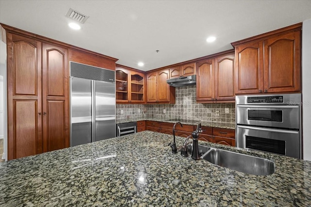 kitchen featuring sink, backsplash, stainless steel appliances, beverage cooler, and dark stone counters