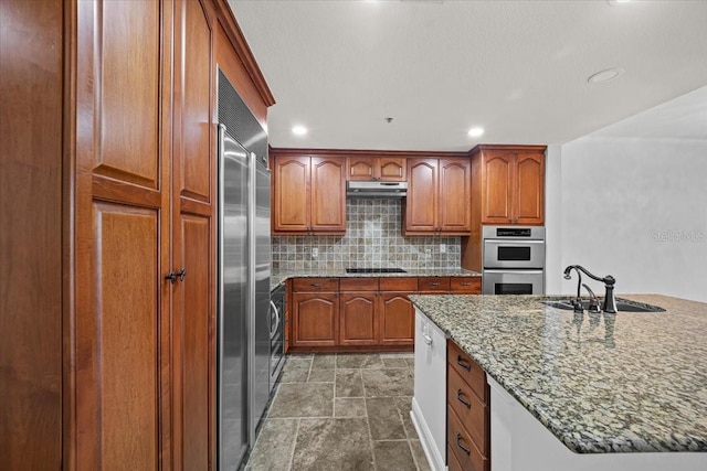 kitchen with sink, decorative backsplash, a kitchen island with sink, light stone counters, and stainless steel appliances