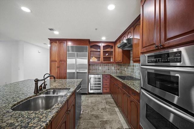 kitchen with sink, appliances with stainless steel finishes, stone countertops, decorative backsplash, and beverage cooler