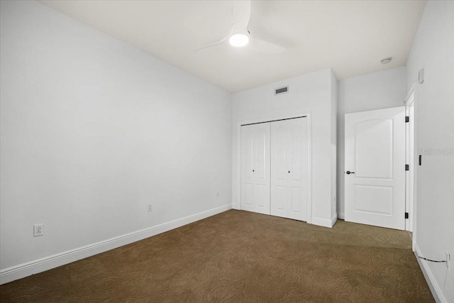 unfurnished bedroom with ceiling fan, dark carpet, and a closet