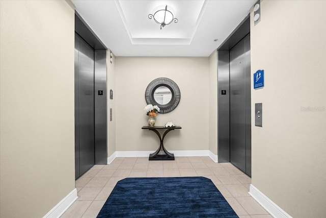 hallway with light tile patterned floors, a tray ceiling, and elevator