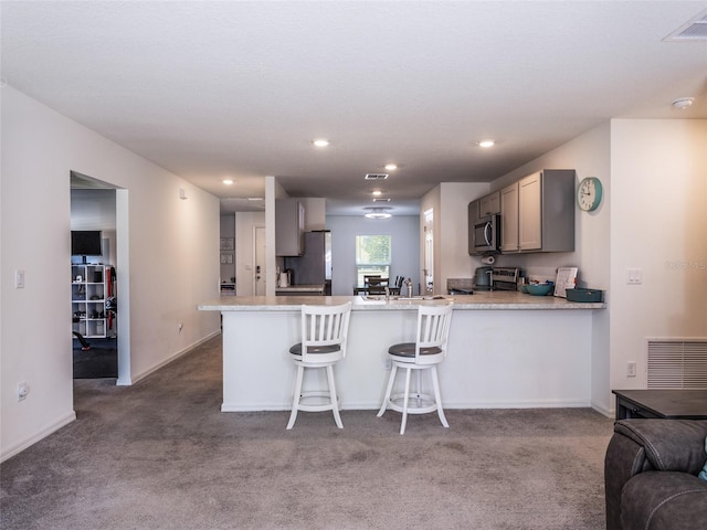 kitchen with gray cabinets, a breakfast bar area, stainless steel appliances, and kitchen peninsula