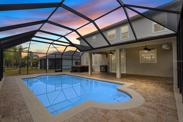 pool at dusk featuring a hot tub, a lanai, ceiling fan, and a patio area