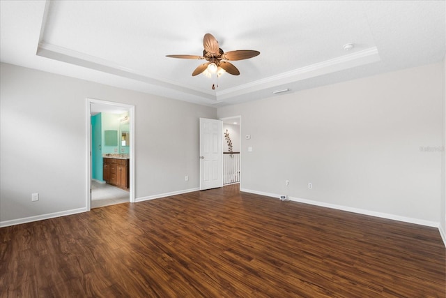 unfurnished bedroom with ensuite bathroom, ceiling fan, dark hardwood / wood-style flooring, and a tray ceiling