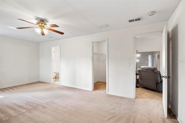 unfurnished bedroom with connected bathroom, a spacious closet, light carpet, a textured ceiling, and a closet