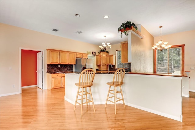 kitchen with stainless steel refrigerator with ice dispenser, an inviting chandelier, decorative light fixtures, light hardwood / wood-style flooring, and decorative backsplash