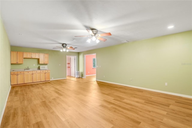 unfurnished living room with sink, light hardwood / wood-style flooring, and ceiling fan