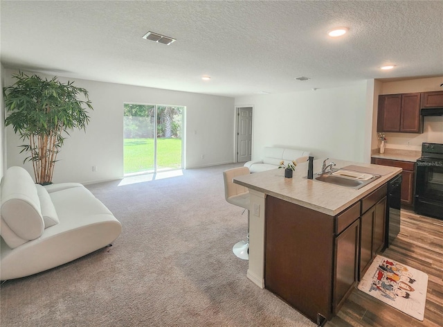 kitchen with sink, a textured ceiling, a center island with sink, carpet floors, and black appliances