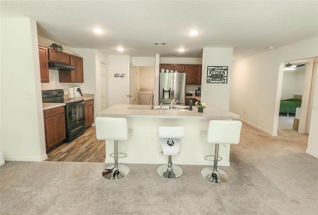 kitchen with a kitchen island with sink, black / electric stove, stainless steel fridge, and a kitchen bar