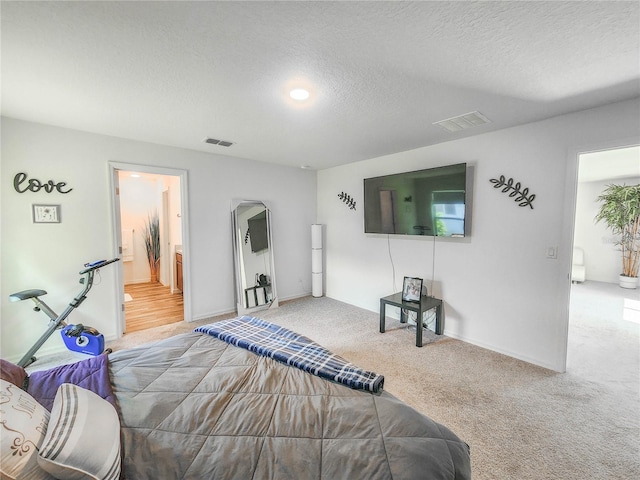 carpeted bedroom with ensuite bathroom and a textured ceiling