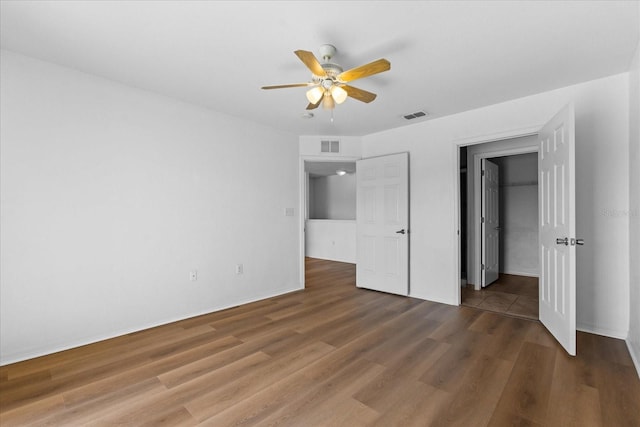 unfurnished bedroom with a walk in closet, dark wood-type flooring, ceiling fan, and a closet