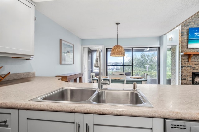 kitchen with sink, dishwasher, hanging light fixtures, white cabinets, and a brick fireplace