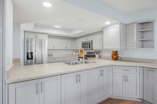 kitchen with appliances with stainless steel finishes, a raised ceiling, sink, and gray cabinetry