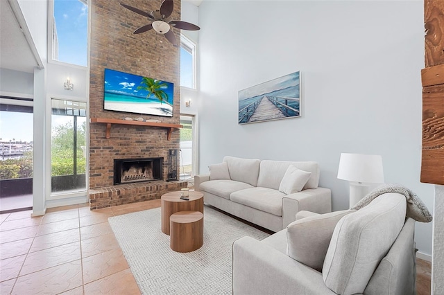 living room with ceiling fan, plenty of natural light, a brick fireplace, and a high ceiling