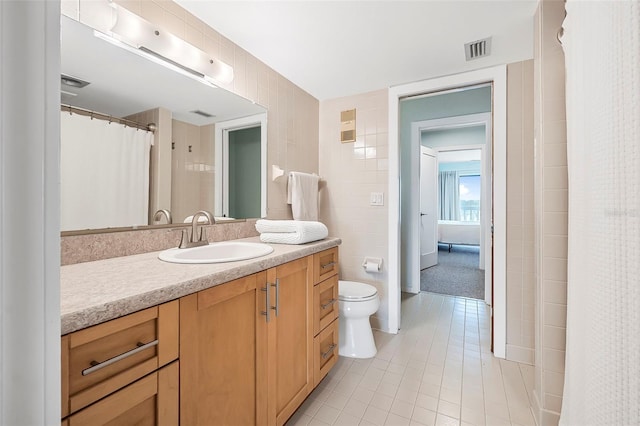 bathroom with tile patterned floors, vanity, toilet, and tile walls