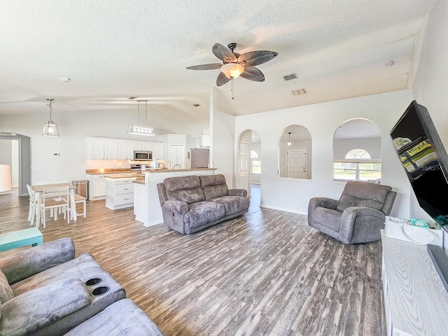 living room featuring hardwood / wood-style floors, vaulted ceiling, a textured ceiling, and ceiling fan