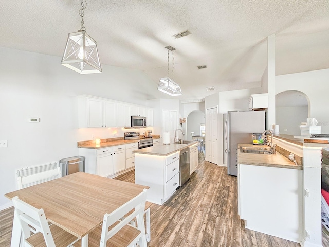 kitchen featuring a center island with sink, stainless steel appliances, hanging light fixtures, and white cabinets