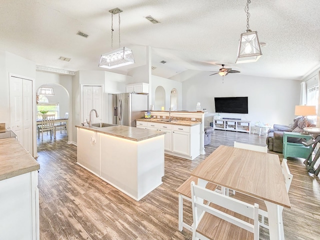 kitchen featuring white cabinetry, stainless steel fridge with ice dispenser, a textured ceiling, hanging light fixtures, and a center island with sink