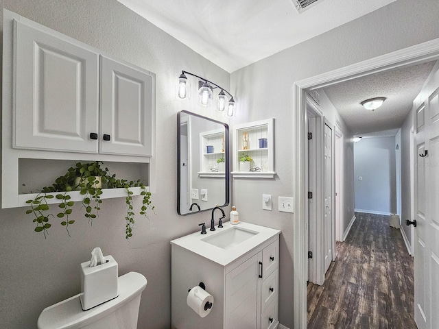 bathroom with hardwood / wood-style flooring, vanity, toilet, and a textured ceiling