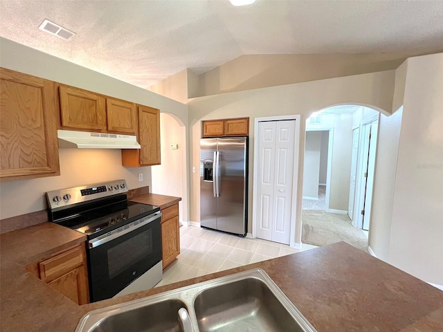 kitchen with sink, vaulted ceiling, a textured ceiling, light tile patterned floors, and stainless steel appliances