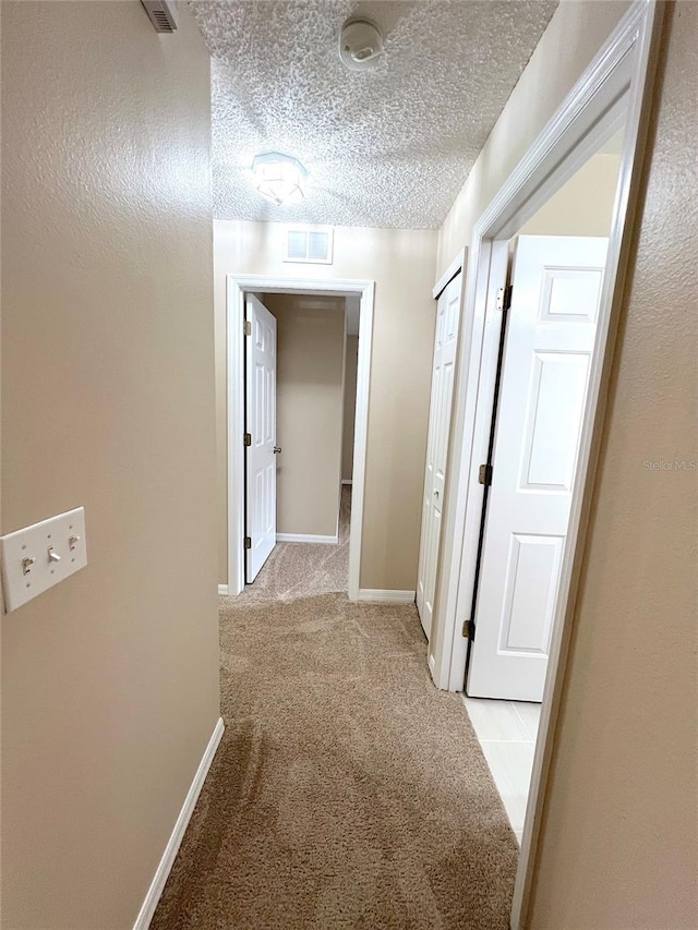 hallway featuring light carpet and a textured ceiling