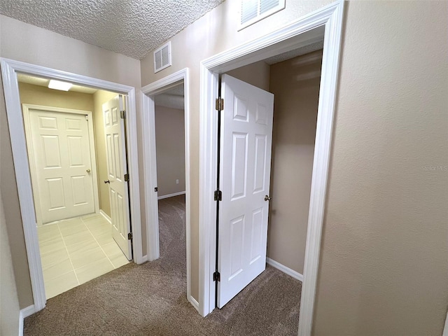 corridor with light colored carpet and a textured ceiling